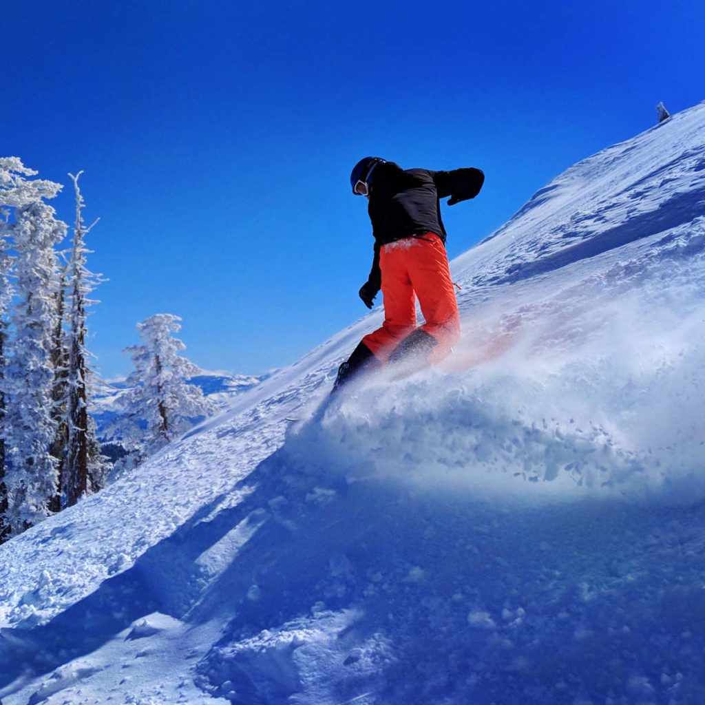 Snowboarder cutting a tight turn in deep powder snow at the top of Sugar Bowl ski resort